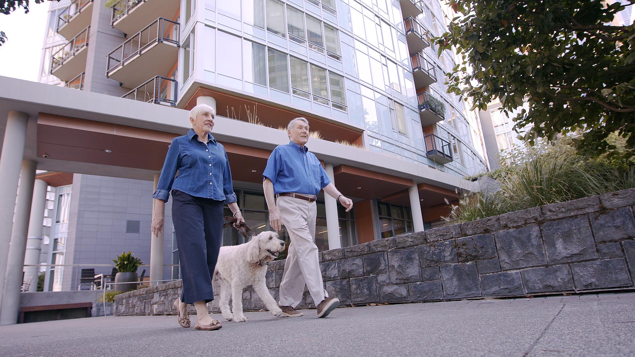 Low-angle shot of a man and woman walking a dog in front of Mirabella Portland.