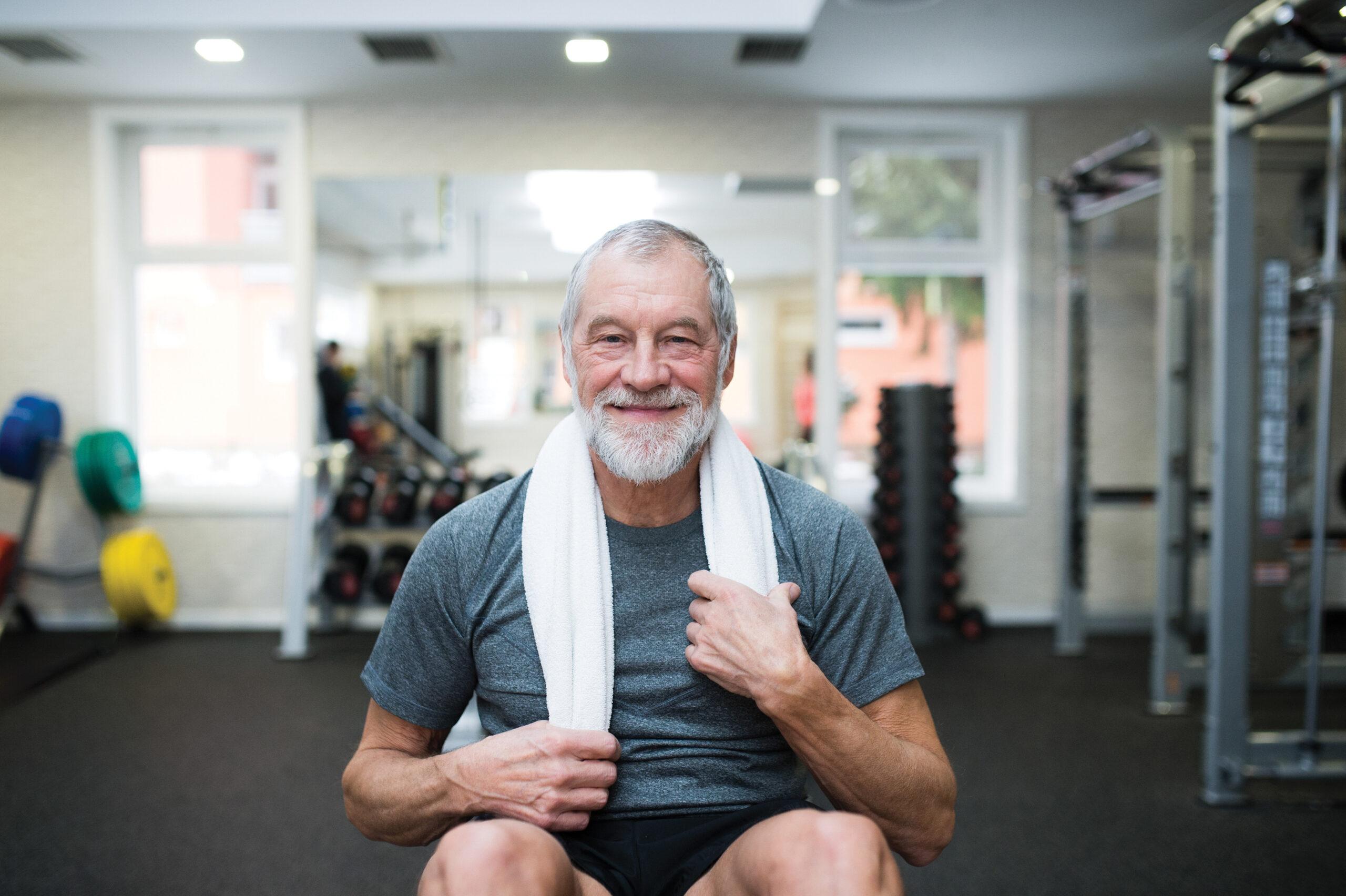 Portrait of a smiling man sitting in a gym with a towel around his neck.