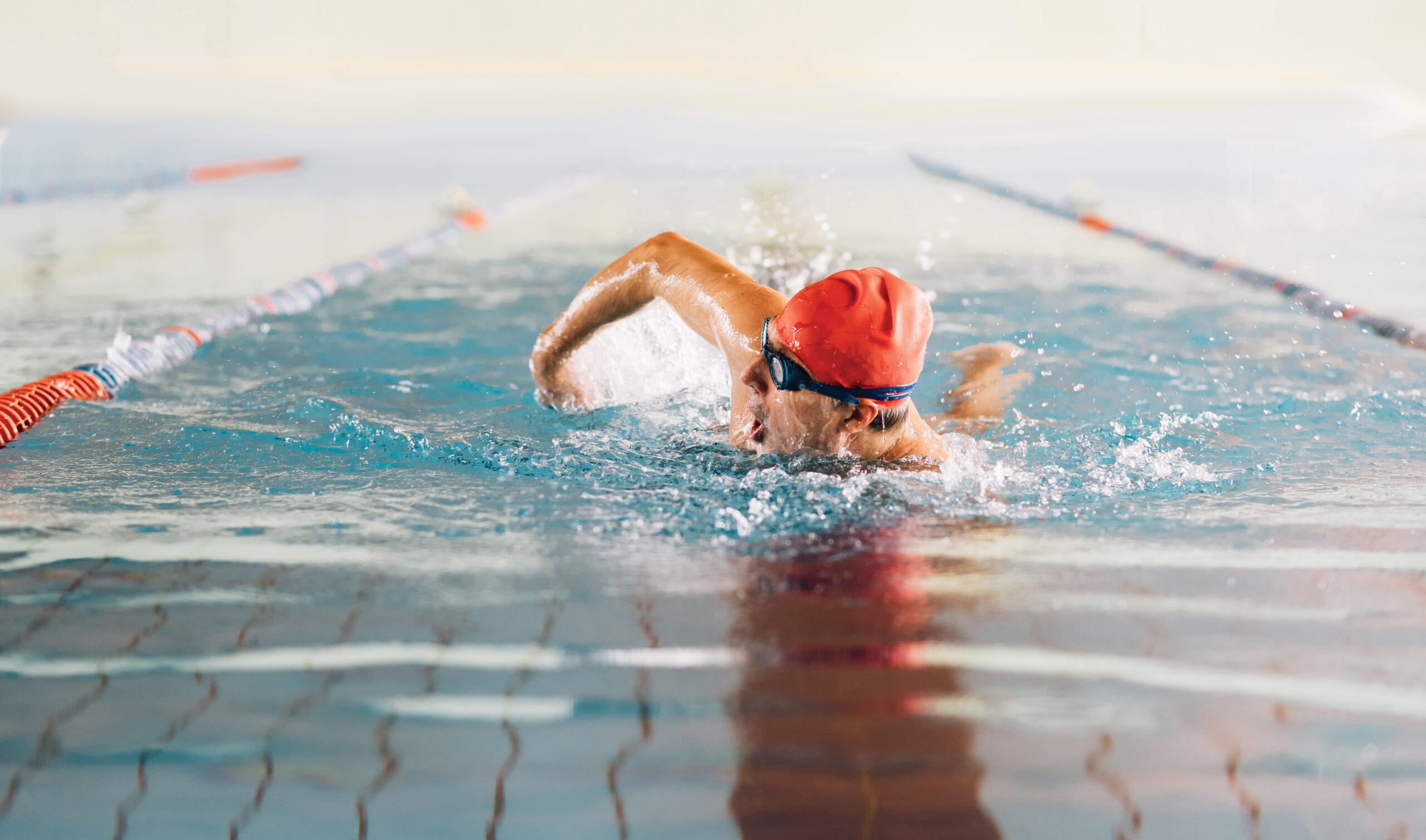 Photo of a man wearing a swim cap and goggles swimming in a pool.