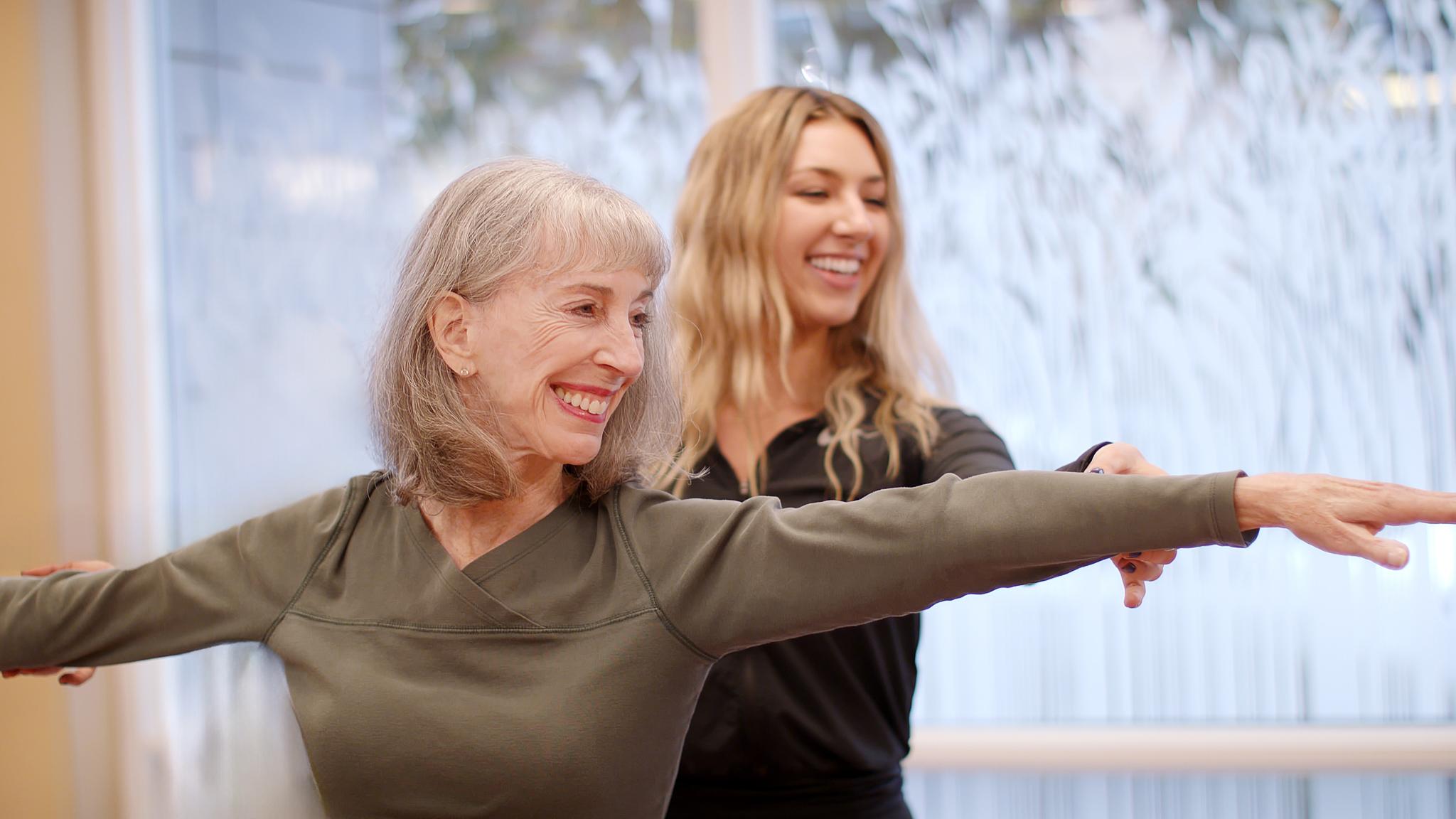 An instructor helps an older woman with her yoga form.