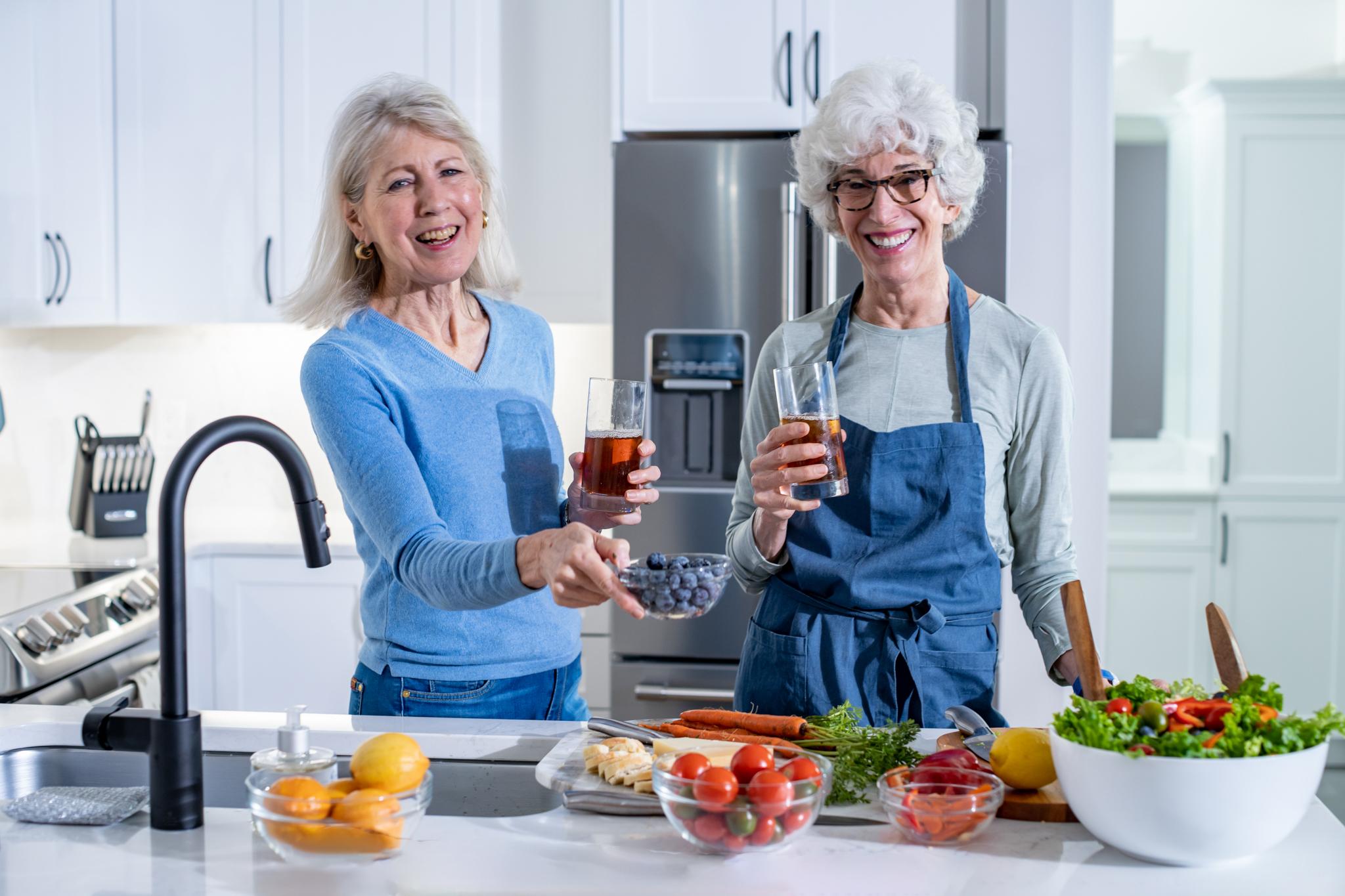 Two women smile as they prepare a variety of healthy foods.