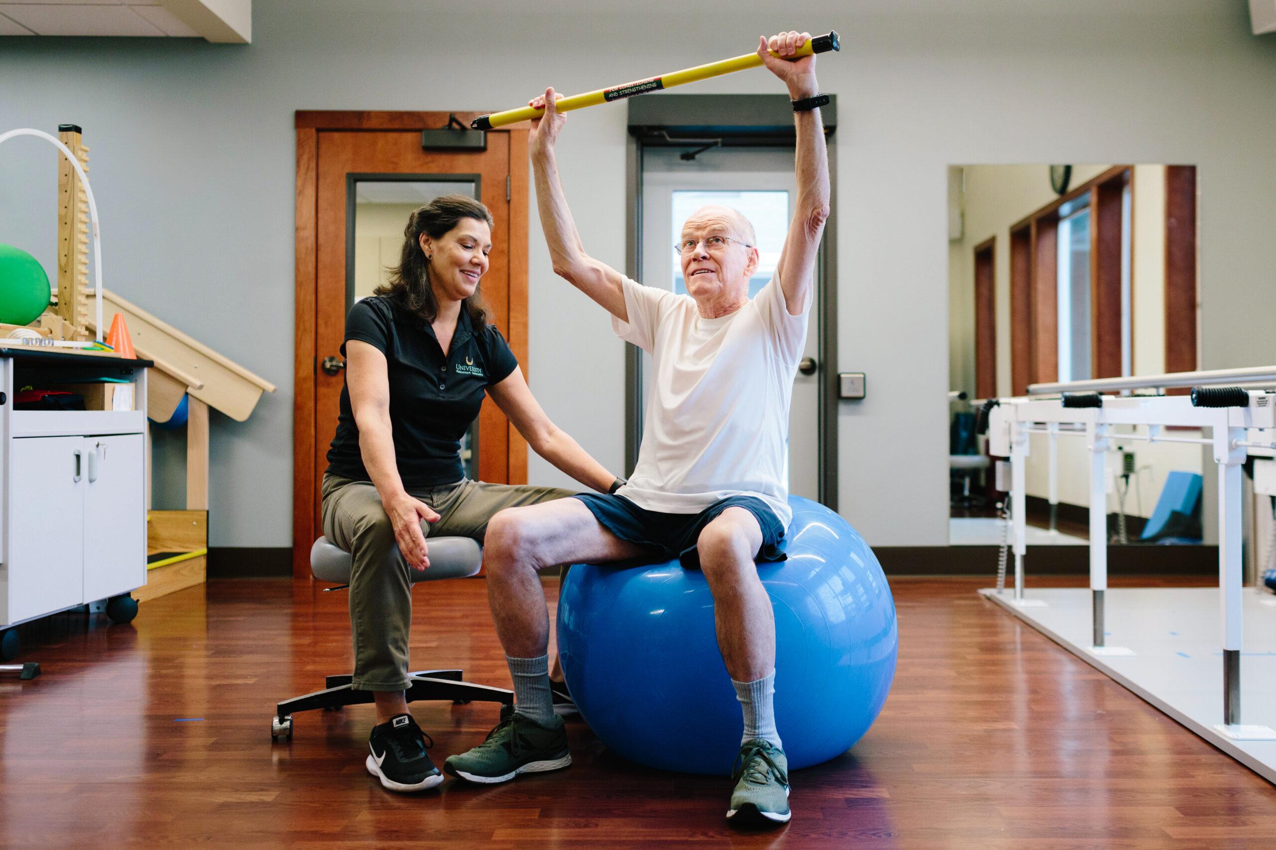 A physical therapist helps an older man with a stretching exercise.